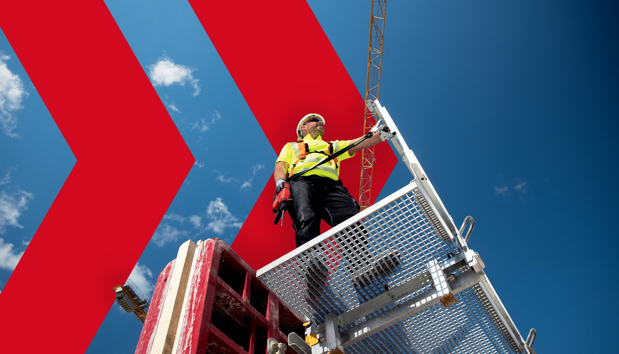 Worker standing on a platform with a drill in his hand that is fixed to a pole with a tool tether